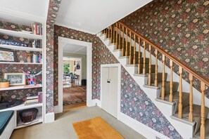 Eine Treppe mit floralem Wanddesign, ein Bücherregal mit Büchern und ein kleiner Teppich.
