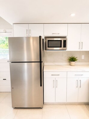 A kitchen with stainless steel appliances, white cabinets, and a potted plant on the countertop. - Grand King Suite | 5-10 Min to Airport & Downtown (Vancouver)