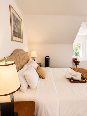 A neatly made bed with white linens, a bedside lamp, and a tray with folded towels. - Grand King Suite | 5-10 Min to Airport & Downtown (Vancouver)