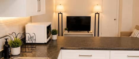 A modern kitchen with white cabinetry, a stainless steel sink, a microwave, and two floor lamps.