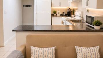 A modern kitchen with white cabinets, a central island, and a beige sofa with patterned cushions.