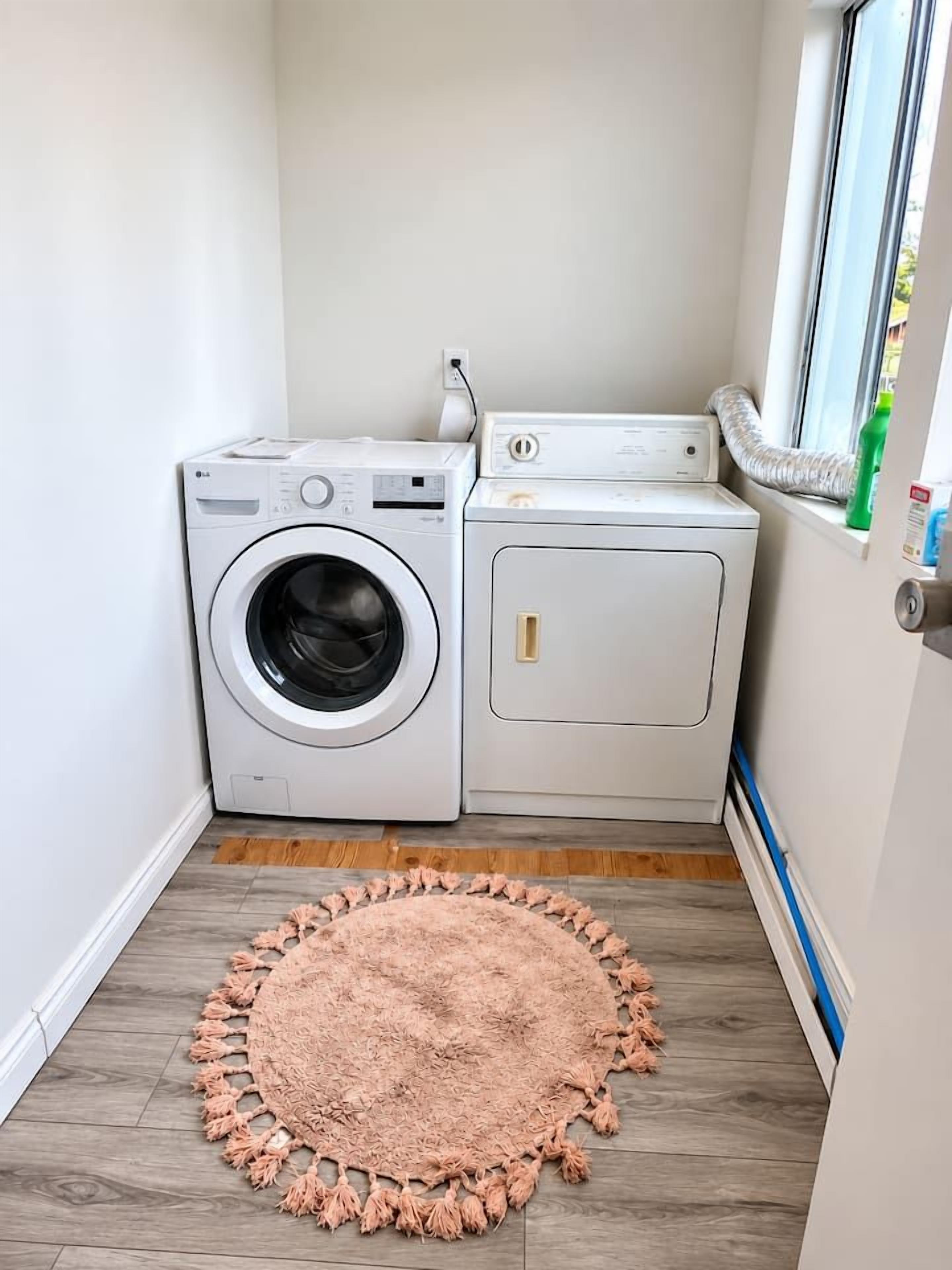 A laundry area with a washing machine and dryer, a wooden floor, and a pink rug.
