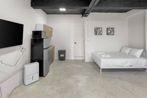 Ein schlicht eingerichtetes Schlafzimmer mit einem Bett, einer kleinen Küchenzeile und einem an der Wand befestigten Fernseher.