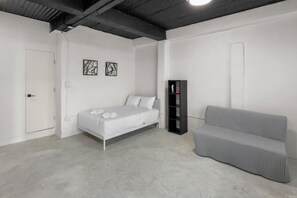 A bedroom with a bed, a grey sofa, a wardrobe, and two wall-mounted artworks. - Casa Magnolia Apt 10 | Studio Apt in Santurce (San Juan de Puerto Rico)