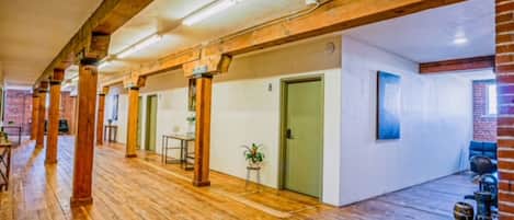 A corridor with wooden flooring, exposed brick walls, and a series of doors.