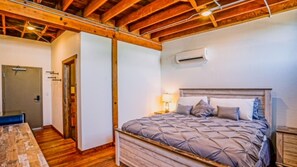 Un dormitori amb sostre de fusta, un llit amb capçalera, una tauleta de nit i un aire condicionat fixat a la paret.