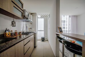 Una cocina moderna con estufa, lavaplatos y armarios. Se observa una ventana con vista a edificios.
