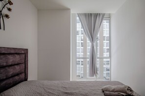 Un dormitorio con cama, ventana con cortinas y vista a un edificio.