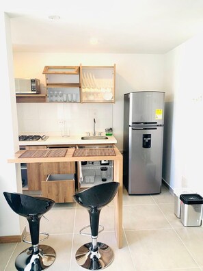 Una cocina compacta equipada con microondas, refrigerador de acero inoxidable, cafetera y espacio para copas de vino.