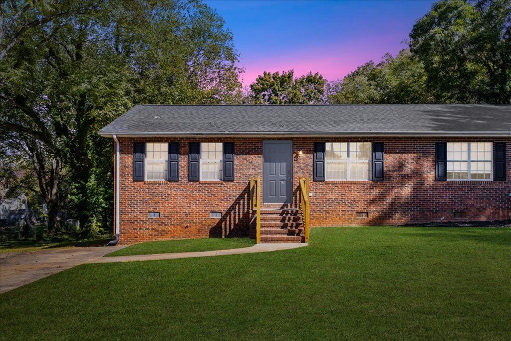 A single-story brick house with a front entrance, a set of stairs leading to the door, and a small front yard.