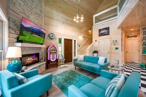 Ein gemütliches Wohnzimmer mit Kamin, Jukebox, großem Fernseher und einer Treppe, die zu einer oberen Ebene führt.