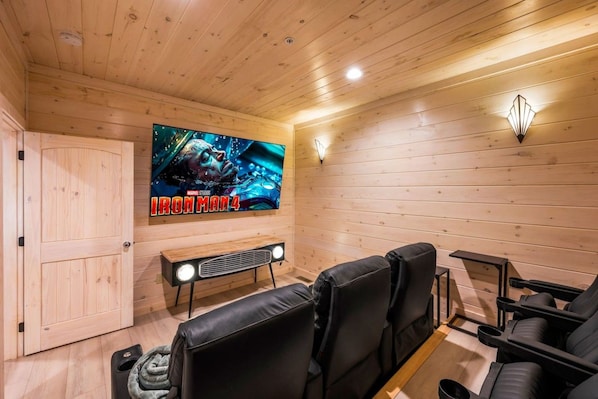 Ein Zimmer mit Holzvertäfelung, einem großen Flachbildfernseher, der 'Iron Man 4' zeigt, einer Bank und schwarzen Ledersitzgelegenheiten.