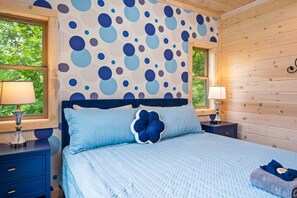 A bedroom with a bed, two bedside tables, and a window with a view of greenery. - Happy Days- Theater/Jukebox/Hot tub/ 2 king suites, Sleeps 10 (Sevierville)