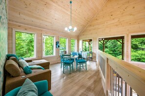 A wooden cabin interior with a dining area, large windows, and a view of the forest. - Happy Days- Theater/Jukebox/Hot tub/ 2 king suites, Sleeps 10 (Sevierville)