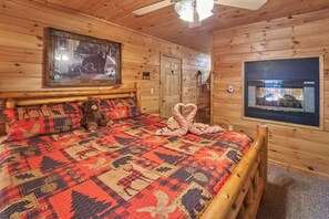 Une chambre à coucher dans un chalet en bois, avec un lit, un ours en peluche, une courtepointe, une cheminée et un tableau encadré accroché au mur.