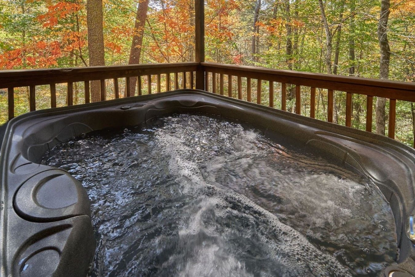 A hot tub with a wooden deck and a forest view.