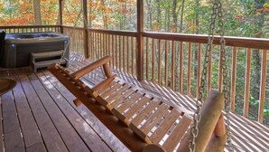 Een houten terras met een hangmat, een jacuzzi en uitzicht op herfstbomen.