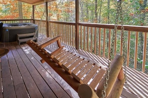 Une terrasse en bois avec un hamac, un jacuzzi et une vue sur les arbres aux couleurs automnales.