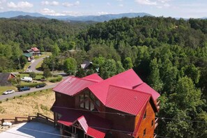 Uma cabana com telhado vermelho, rodeada por uma paisagem arborizada e montanhas ao fundo.