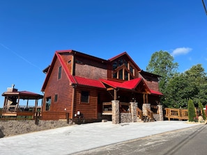 A large log cabin with a red roof, stone foundation, and a porch with wooden railings. - A Rustic Escape-Theater Room/Handicap Ramp/Hot tub/2 fireplaces/2 king suites (Sevierville)