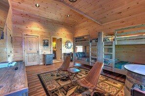 A wooden cabin interior with bunk beds, a dining table, and a clock on the wall. - A Rustic Escape-Theater Room/Handicap Ramp/Hot tub/2 fireplaces/2 king suites (Sevierville)