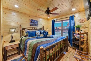 Ein Schlafzimmer einer Holzhütte mit einem Bett, einem Deckenventilator, einem Fenster mit Vorhängen und einem Bücherregal.
