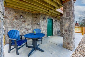 Eine Fassade aus Stein mit einer grünen Tür, eine überdachte Terrasse mit einem runden Tisch und blauen Stühlen sowie eine Steinmauer mit Laternen.