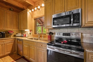A kitchen with wooden cabinets, a stainless steel microwave, and an oven. - Dances with Wolves- Spacious Cabin, Hot tub, Swing, Large yard (Sevierville)