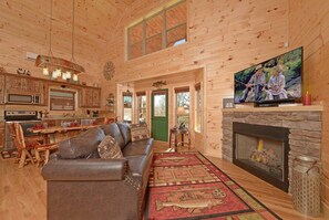 A cozy cabin interior with a fireplace, wooden walls, a leather sofa, and a dining area. - A Barrel of Fun-riverfront cabin, fishing nearby (Pigeon Forge)
