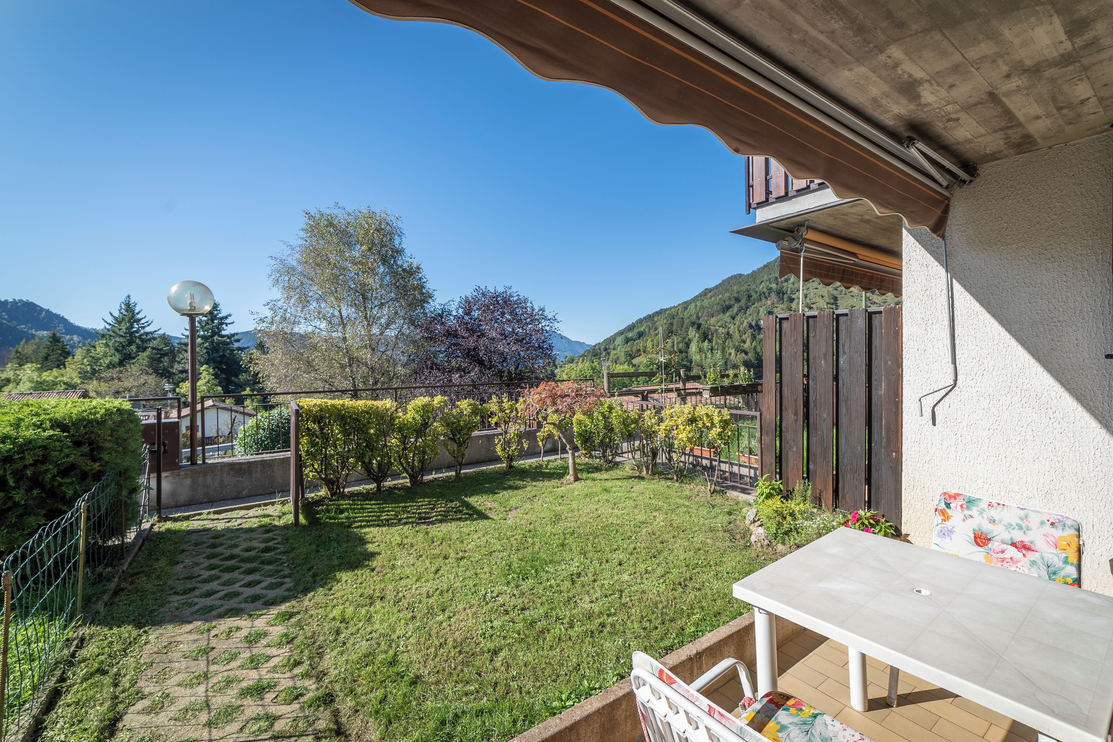 Un patio con mesa y sillas, rodeado por un jardín con diversas plantas y vista a una montaña.