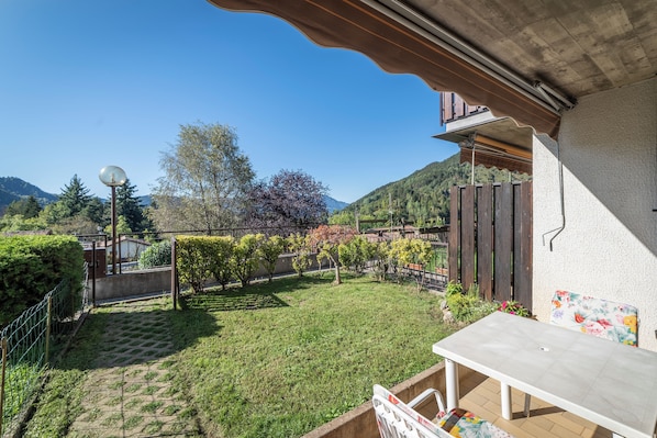A patio area with a table and chairs, surrounded by a garden with various plants and a view of a mountain.