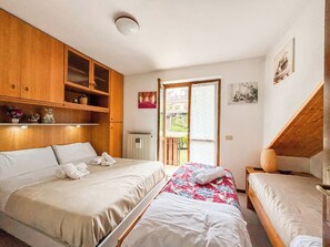 A bedroom with two beds, wooden cabinets, and a balcony.