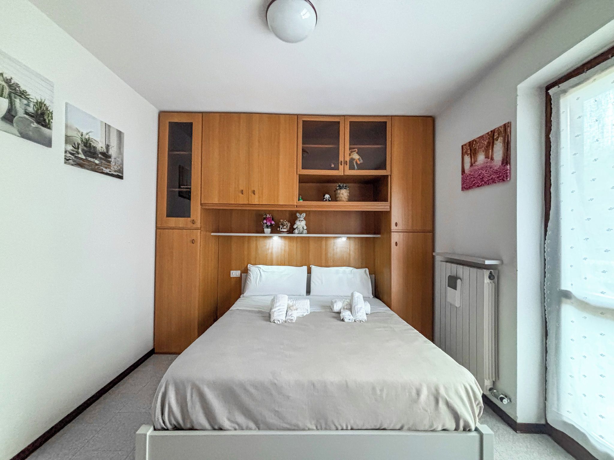 A bedroom with a bed, wooden cabinets, and a radiator.