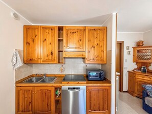 Een praktische keuken met houten kastjes, een roestvrijstalen spoelbak, een vaatwasser en een ingebouwde magnetron.