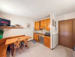 A compact kitchen with wooden cabinets, a built-in oven, and a dining area with a wooden table and chairs.