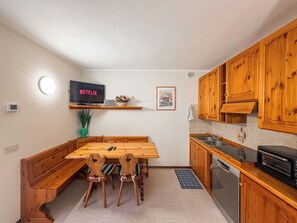A compact kitchen with wooden cabinets, a built-in oven, and a dining area with a wooden table and chairs.