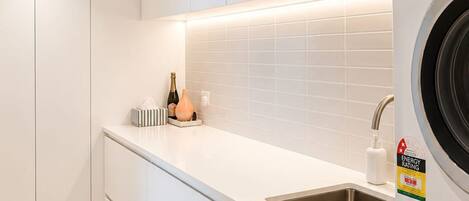 A modern kitchen with a built-in washing machine, a sink, and a countertop with a bottle of champagne and a tissue box.