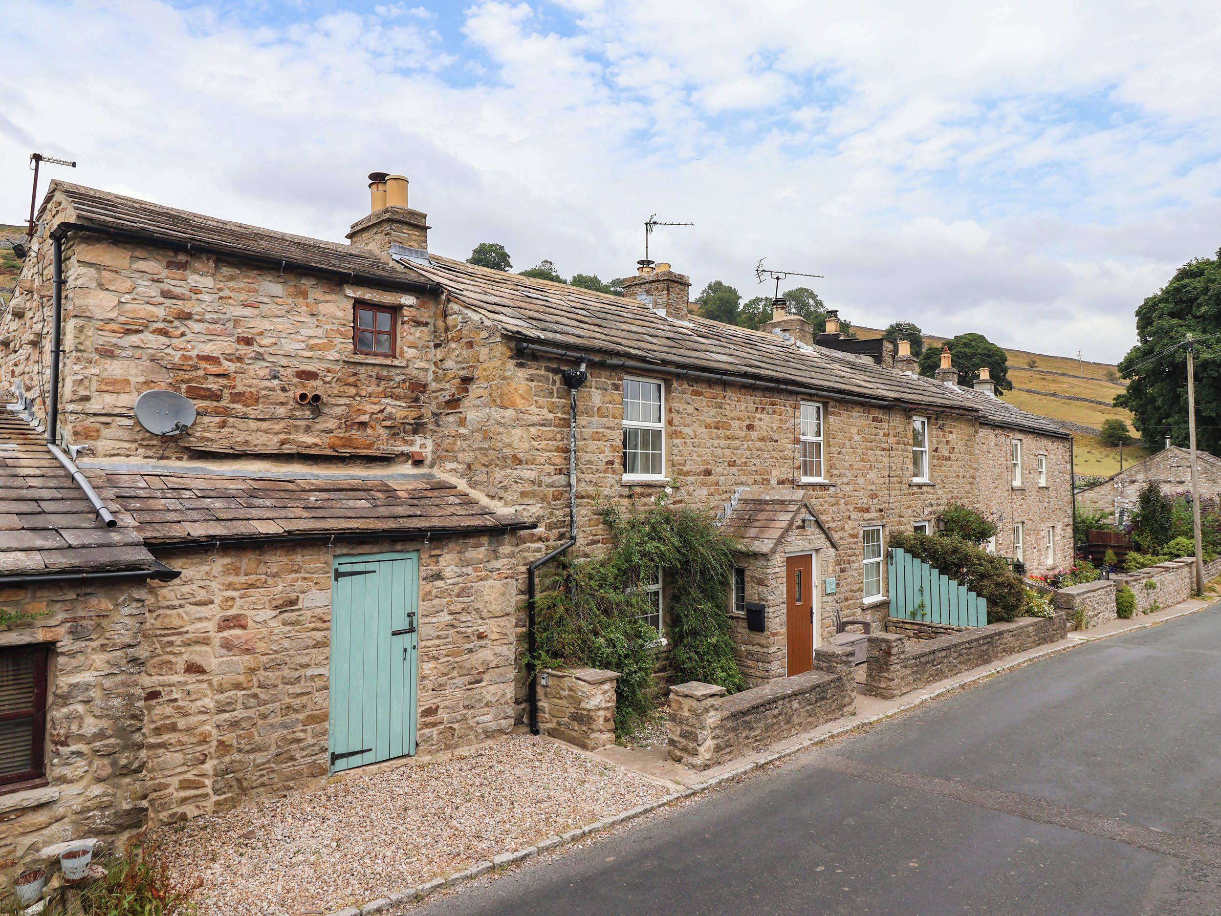 A row of stone houses with a traditional design, featuring a mix of single and double-story structures, a gravel driveway, and a clear sky.