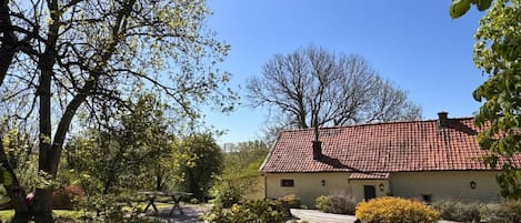 Ein Haus mit roten Ziegeln auf dem Dach, umgeben von Bäumen und einem gepflegten Rasen.