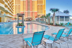 A hotel pool area with a large pool, lounge chairs, and a building with balconies in the background. - Walk to the Beach • Resort Pools • Pier Park (Panama City Beach)