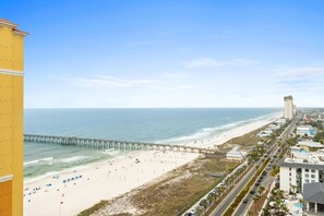 A coastal cityscape with a beach, a pier, and a hotel with a pool. - Walk to the Beach • Resort Pools • Pier Park (Panama City Beach)