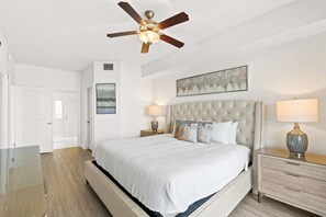 A bedroom with a bed, a ceiling fan, a nightstand, a lamp, and a painting on the wall. - Walk to the Beach • Resort Pools • Pier Park (Panama City Beach)