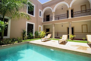 A poolside area with two lounge chairs, a clear swimming pool, and a building with a balcony. - Colonial Mérida Outside, Poolside Relaxation Inside | 2 Beds (Mérida)