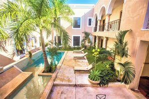 A pool area with lounge chairs, palm trees, and a building with arches and balconies. - Colonial Mérida Outside, Poolside Relaxation Inside | 2 Beds (Mérida)