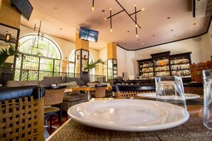 A restaurant with wicker furniture, a bar area with shelves of bottles, and a TV mounted on the wall. - Mérida Made for Groups | 3 Double Beds + Pool (Mérida)