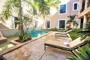 A pool area with lounge chairs and a small pool, surrounded by palm trees and a building with large windows. - Mérida Made for Groups | 3 Double Beds + Pool (Mérida)