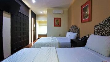 Quarto de hotel com duas camas, uma mesinha de cabeceira, ar condicionado e uma porta com painel de segurança.