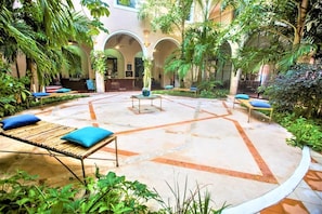 A courtyard with a central seating area, surrounded by lush greenery and arches. - Explore Mérida, Then Take a Dip | Cozy Double Room (Mérida)