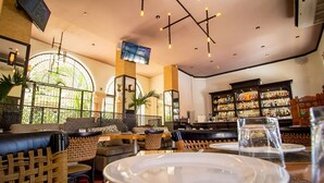 Un restaurant amb mobiliari de vimet, una zona de bar amb estantes plenes de botelles, i un televisor fixat a la paret.