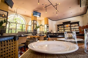 A restaurant with wicker furniture, a bar area with shelves of bottles, and a TV mounted on the wall. - Explore Mérida, Then Take a Dip | Cozy Double Room (Mérida)